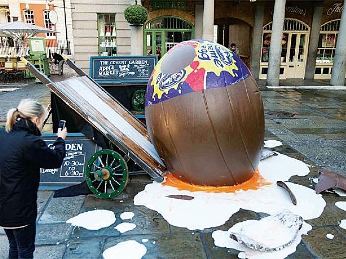 A giant creme egg lies smashed on the ground beside a tilted market barrow.