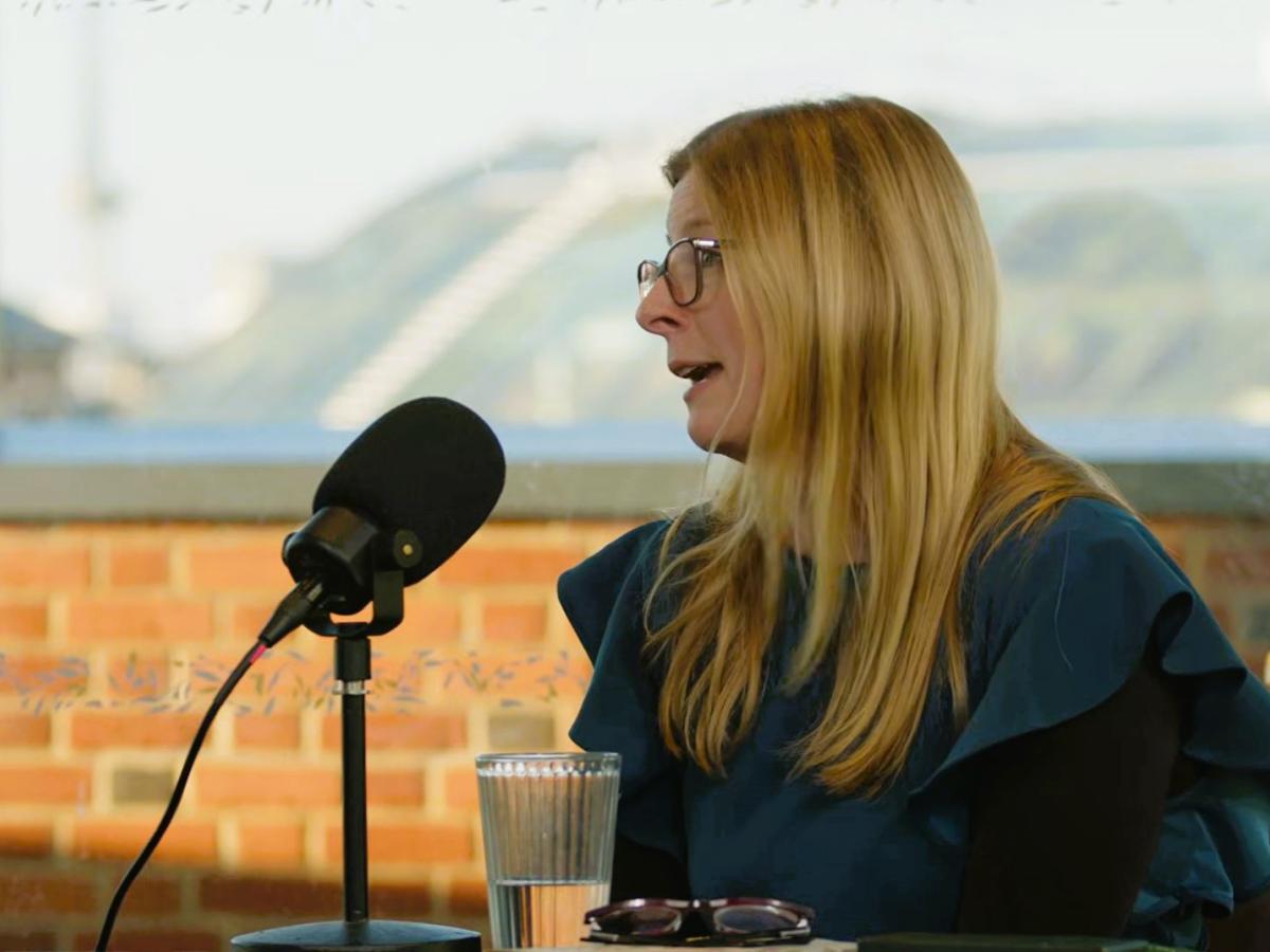 A woman sits at a table and talks with a microphone on a stand in front if her,