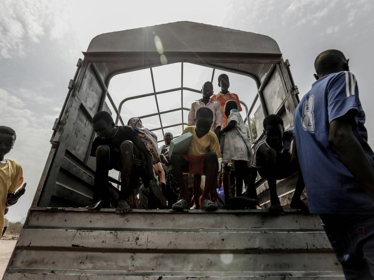 Refugees stand at the back of an open truck.