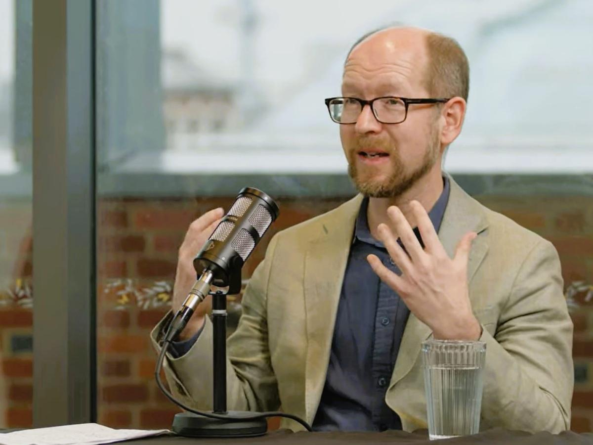 A podcast guest sits in front of a mic, gesturing with their hands.