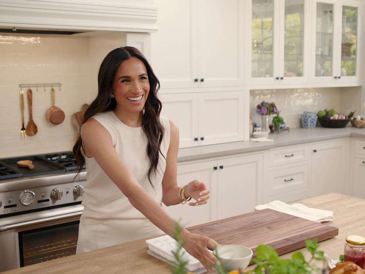 A woman stands at a kitchen island with a chopping board on it.