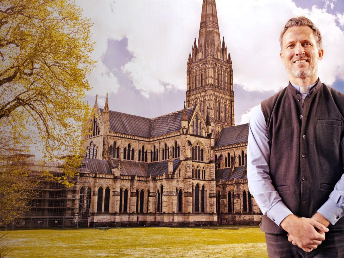 A vicar stands arms in front of himself, behind him is a cathedral