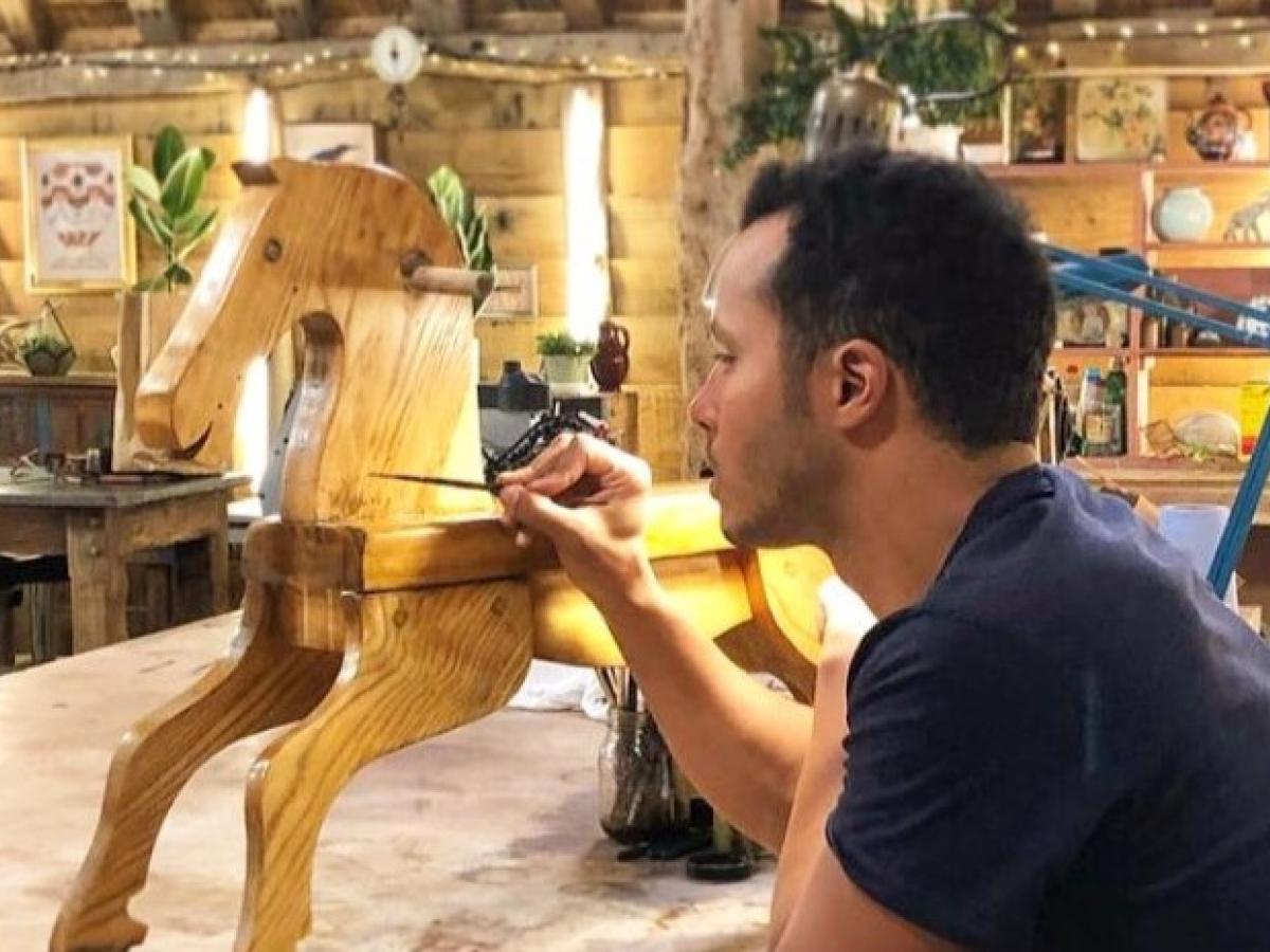 A restorer rest on his elbows while painting a wooden rocking horse.