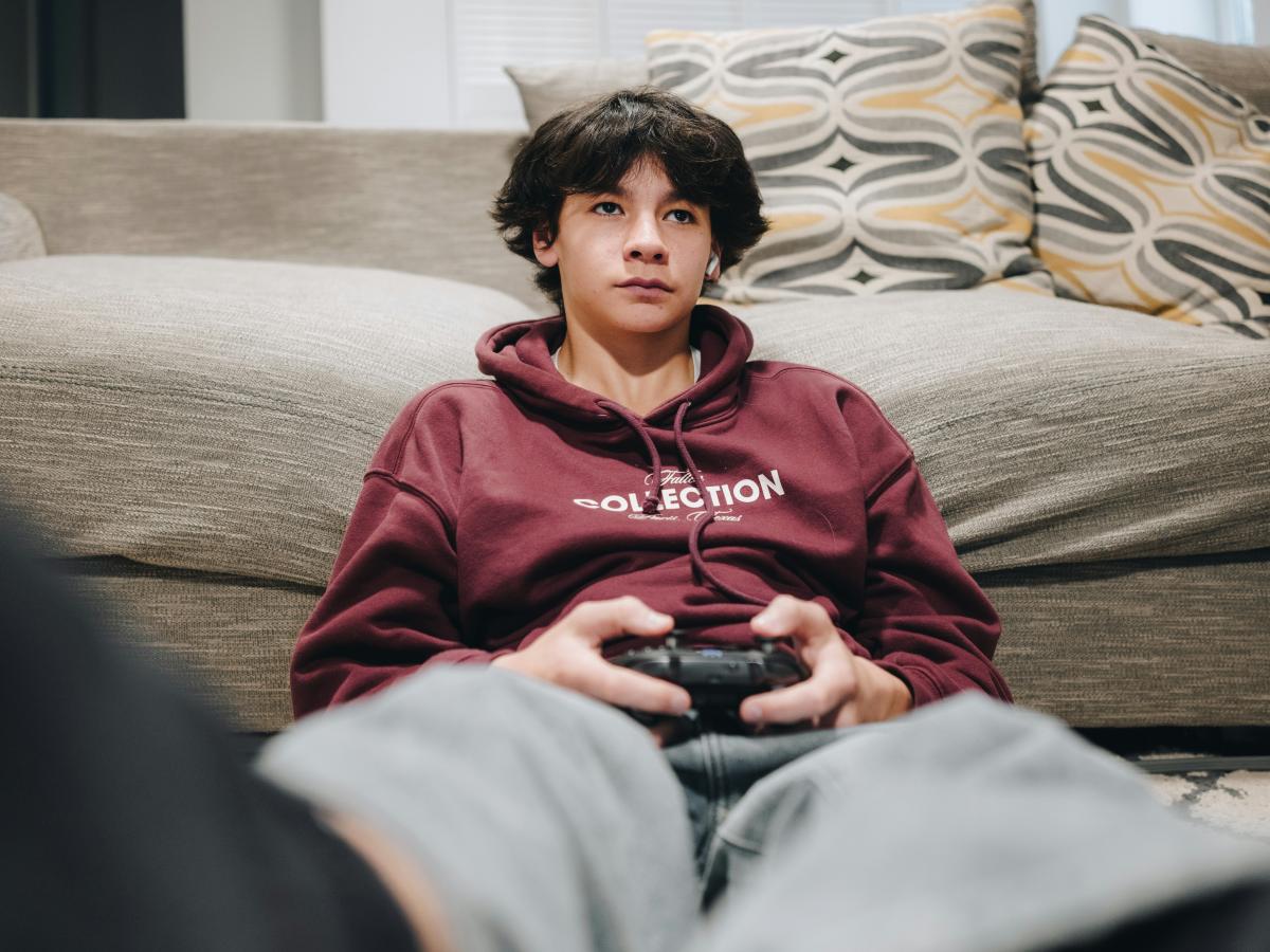 A teenager slumped against a sofa plays a video game
