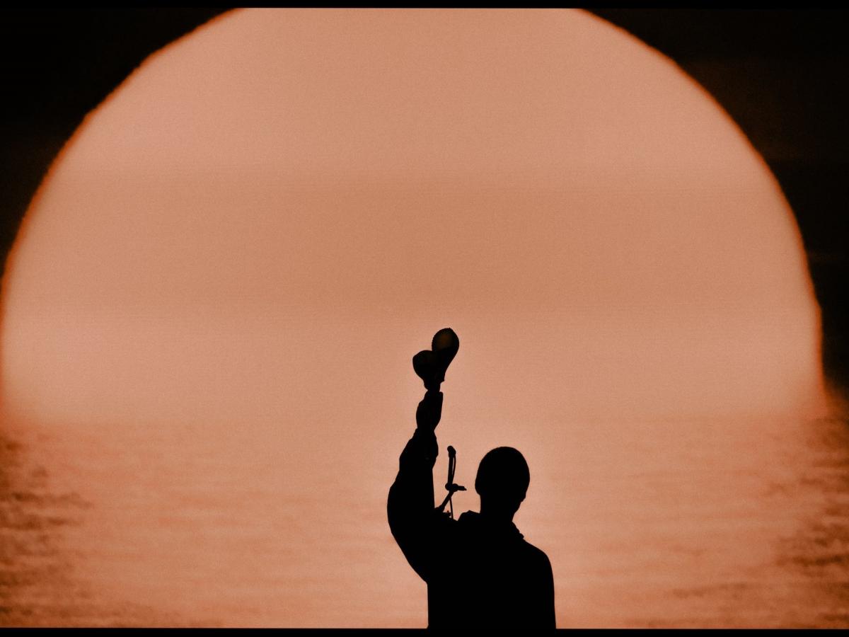 A silhouette of a musician holding up shakers.