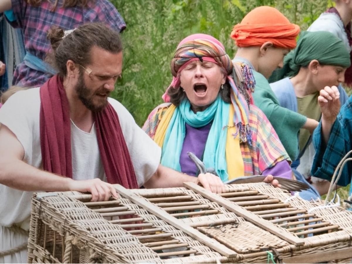 An outdoor theatrical setting shows Jesus with a basket.