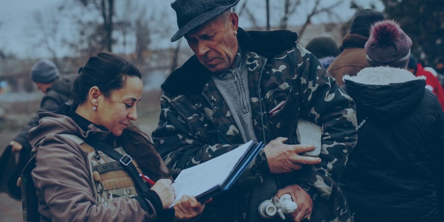 An aid worker and a local resident consult a list as they stand outside in a battle-affected town.