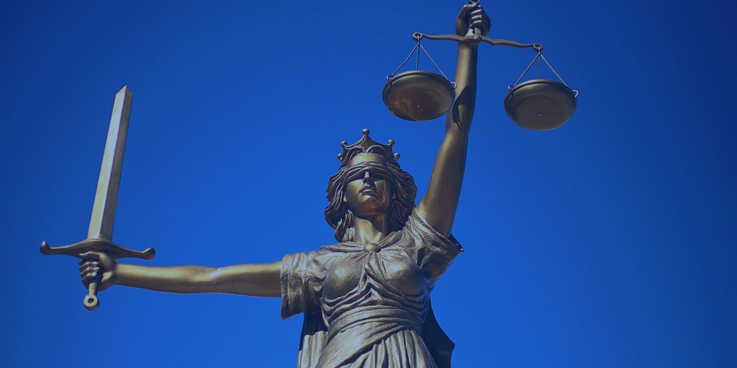 A statue of Justice holds a sword aloft in one hand, and set of scales in the other.