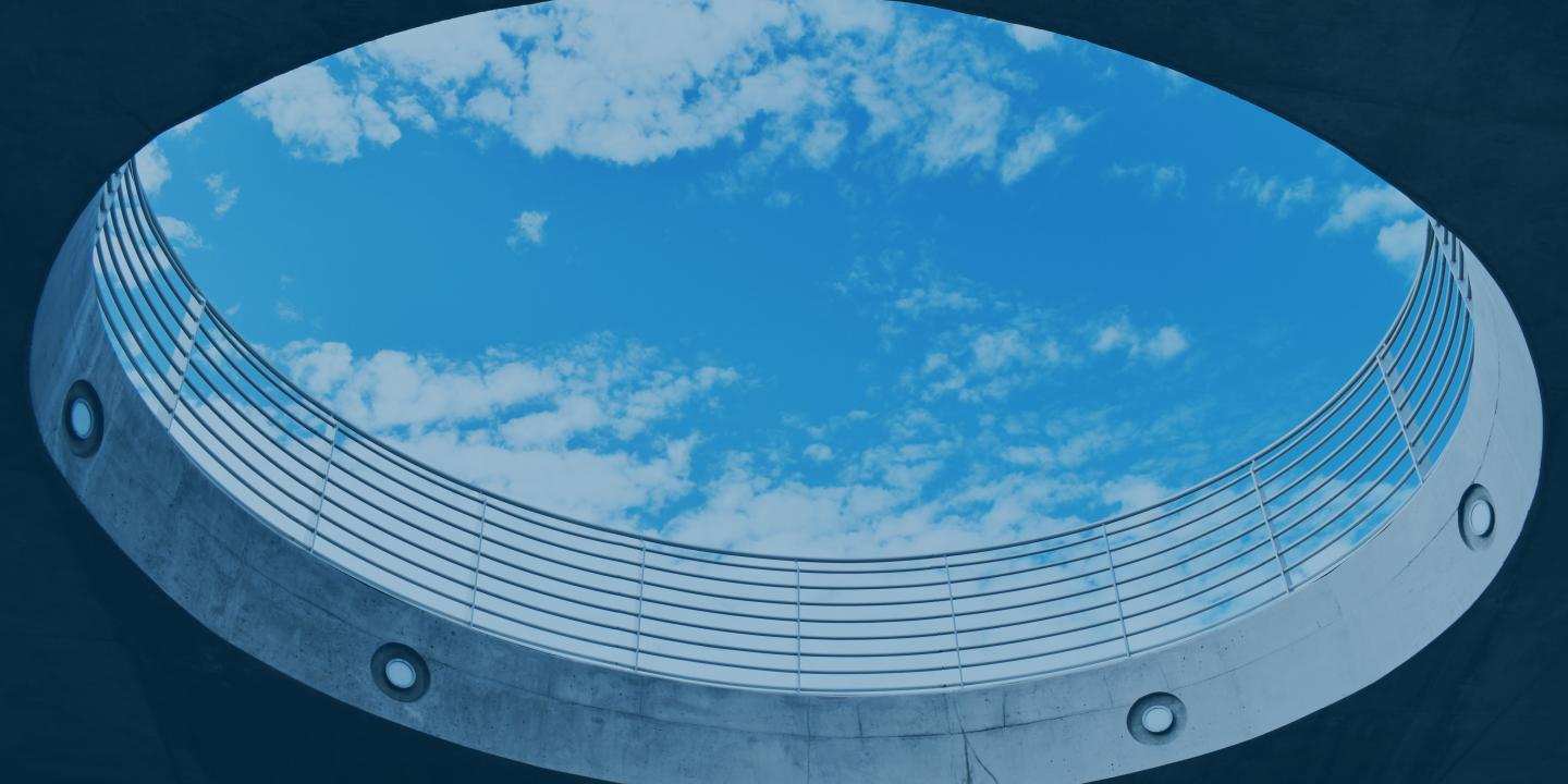 A cloud-dappled s blue sky is viewed through a large circular opening, from below.  