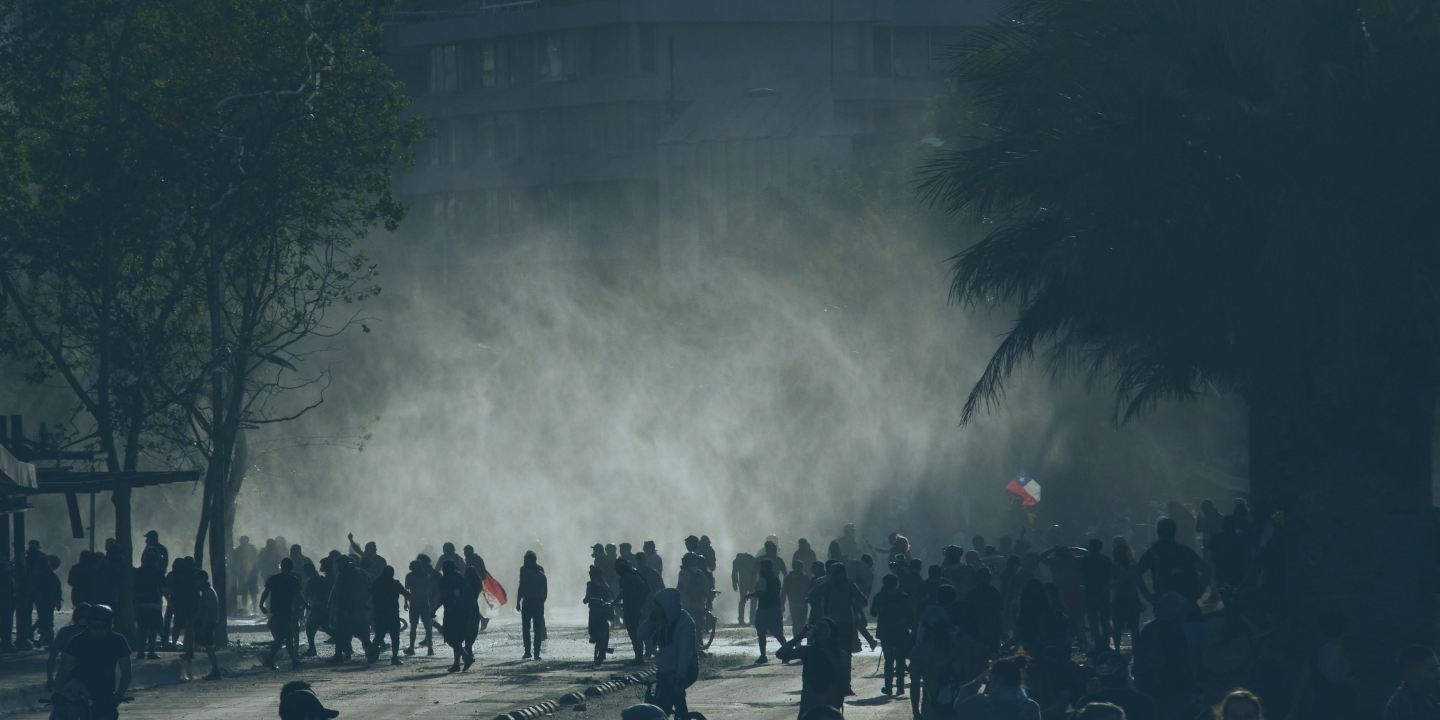 A loose rabble of a protest in the street is siluhetted against light and a shower of rain