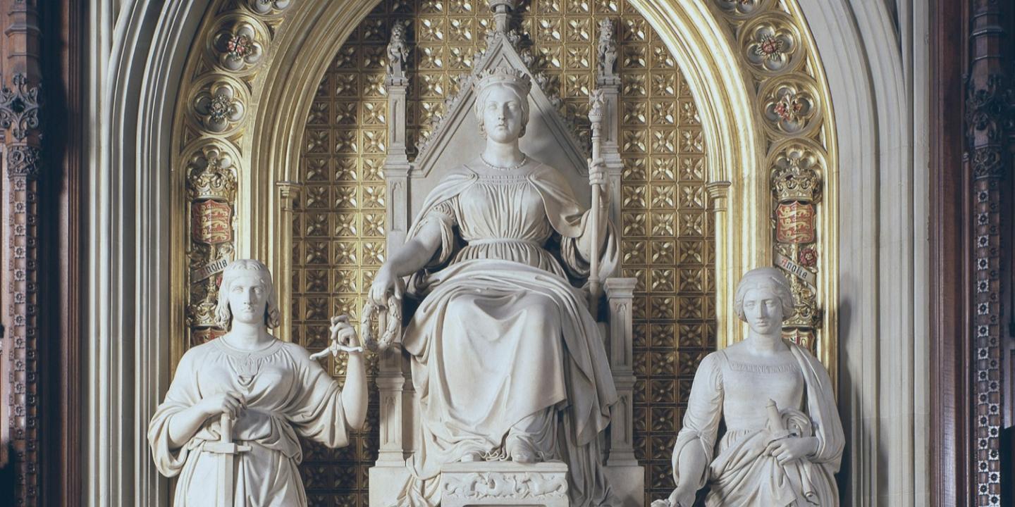 Under a gilded arch, a statue of a young Queen Victoria sits, between two standing figures.