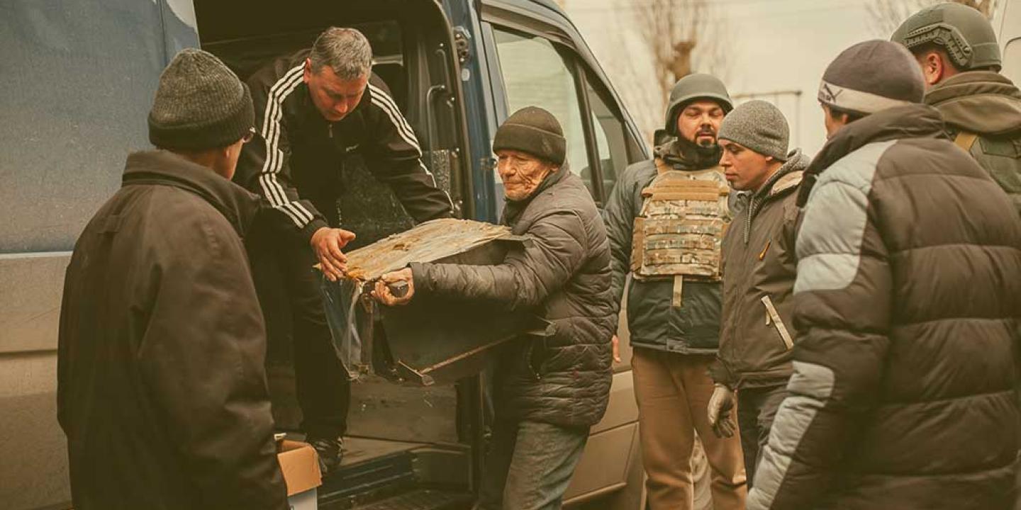 People help unload aid parcels from the side of a van, some wearing body armour.