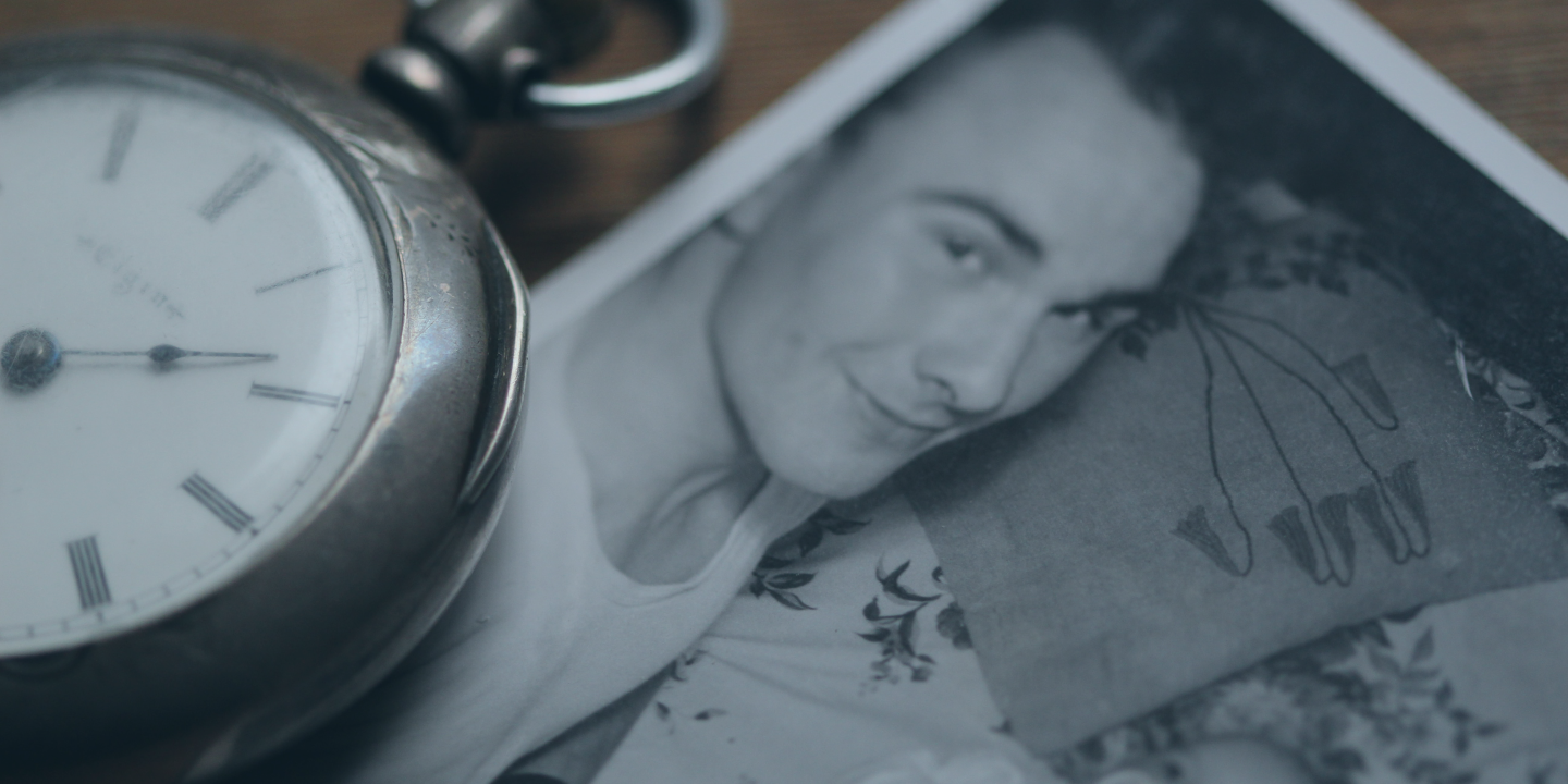 A pocket watch rests next to a black and white photograph of a father lying beside a new born baby.