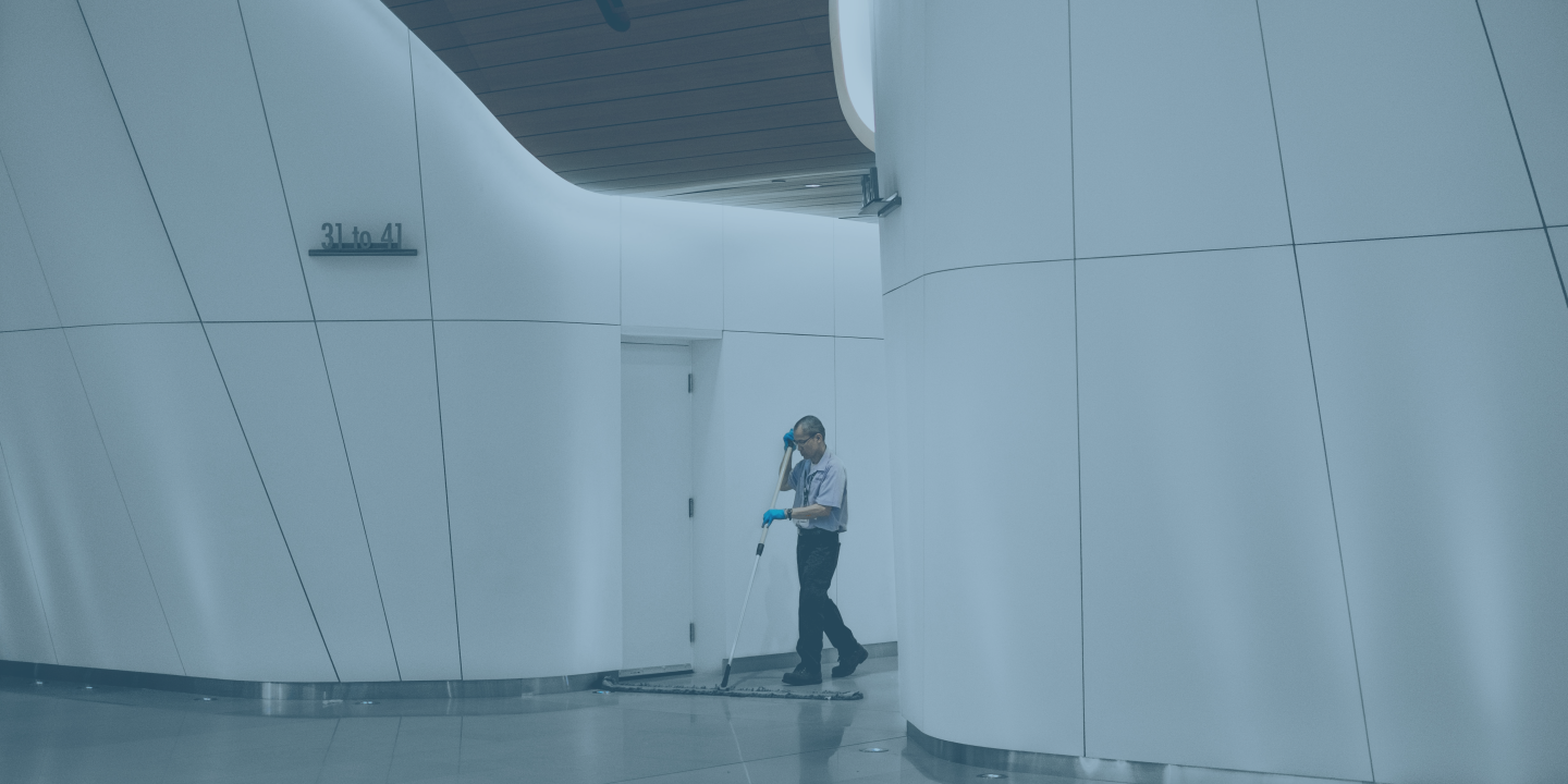 A cleaner sweeps between large white interior walls of a concourse.