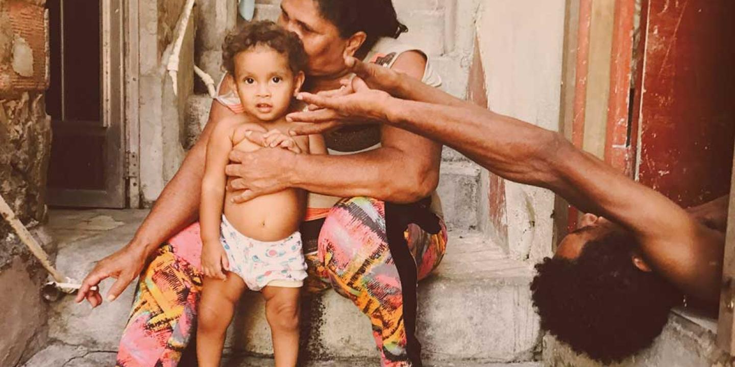 A mother sits with a toddler standing in front of her. The father appears from the side lying on his back reaching an arm out.