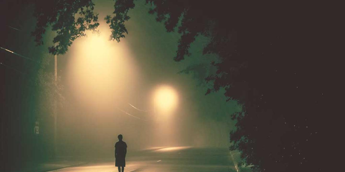 A person stands in a road under misty street lights.