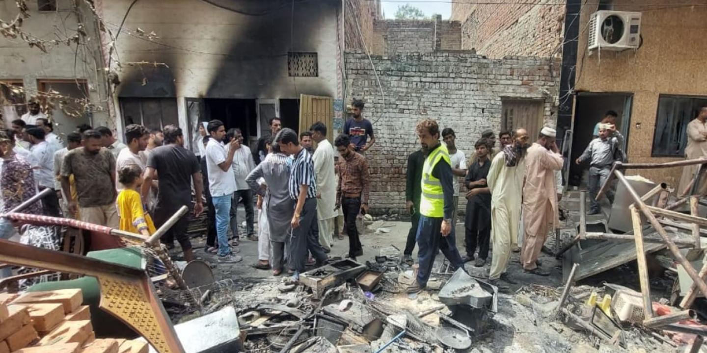 A crowd of people inspect fire damaged debris outside a burnt-out church.