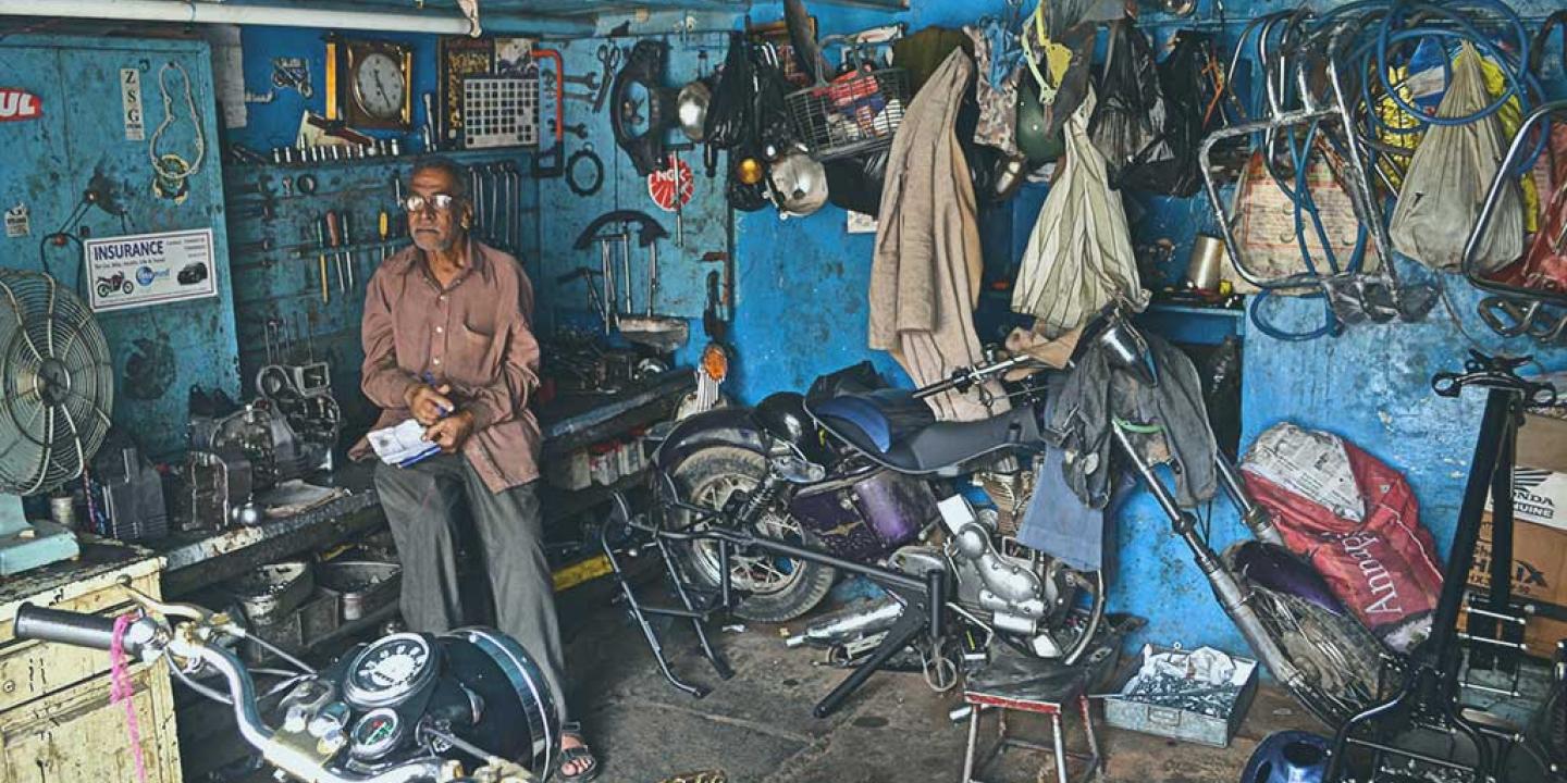 A mechanic stands in a workshop beside a motorcycle under repair.