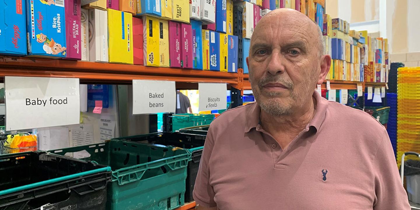 A man stands in front of a food bank's shelves of cereals and boxes labelled by foot type.