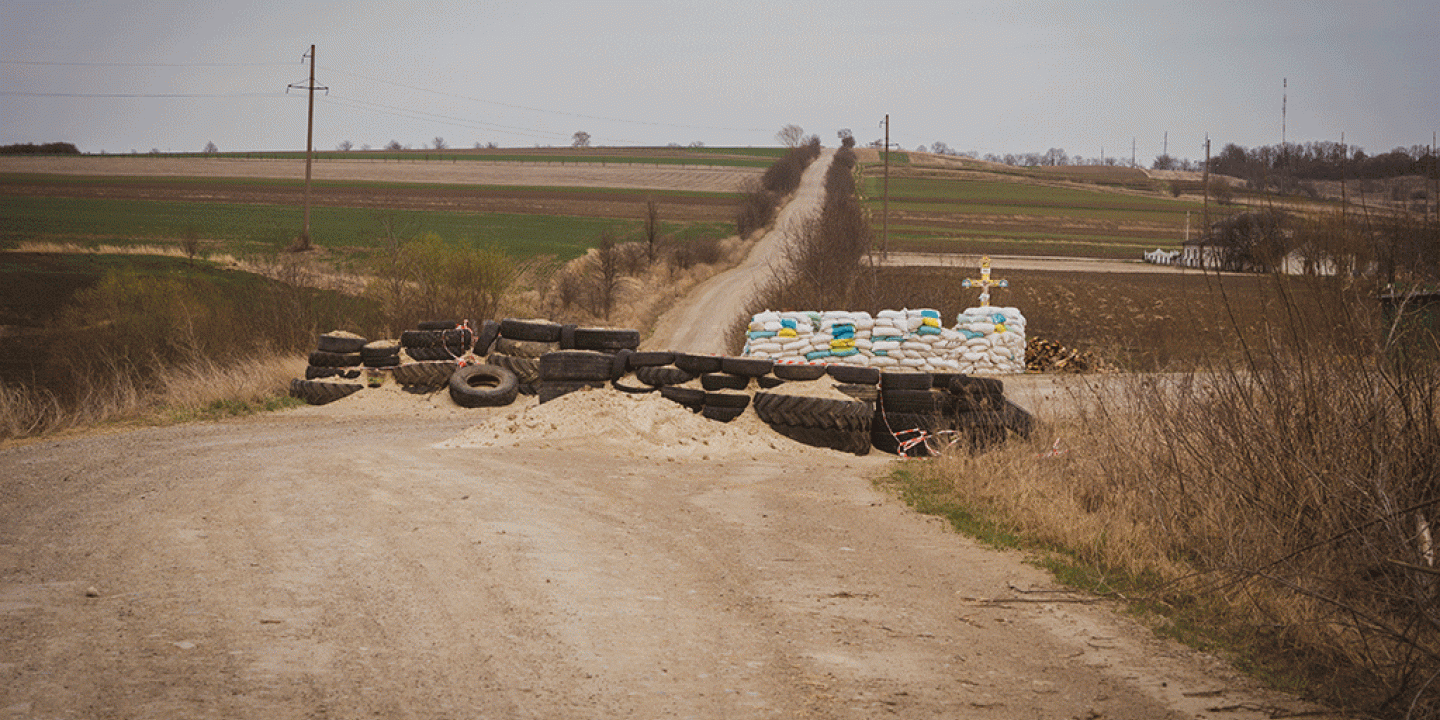 a dirt barricade blocks a cross roads, behind which stands a roadside cross