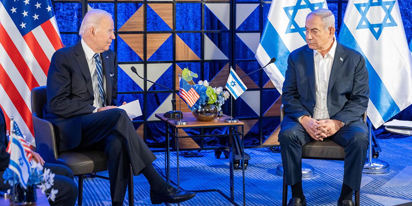 Two country leaders sit in chairs next to each other with their country's flags behind