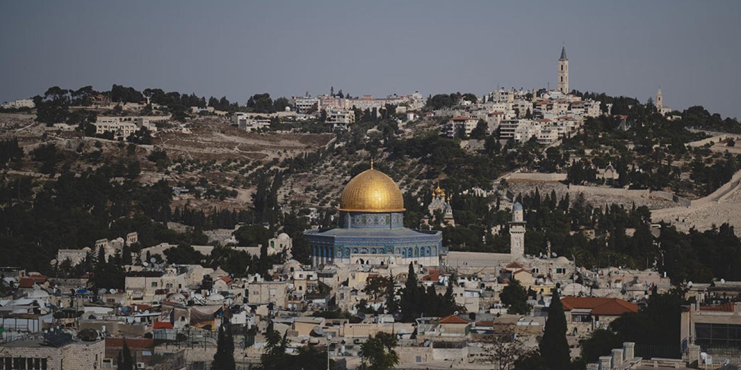 A blue and gold domed mosque sits surrounded by old stone buildings of a city.