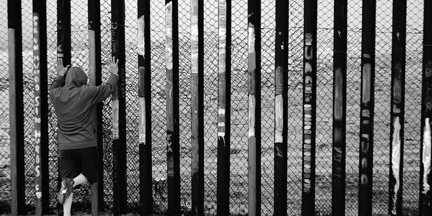 A person holds the vertical tall steel bars of a border fence.