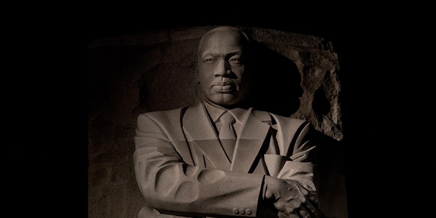 An imposing stone statue of Martin Luther King standing with his arms crossed.