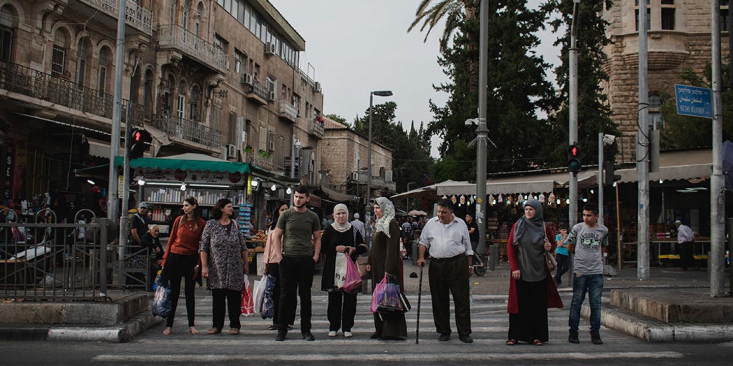 A line of people, some old, some young, wait to cross a road.