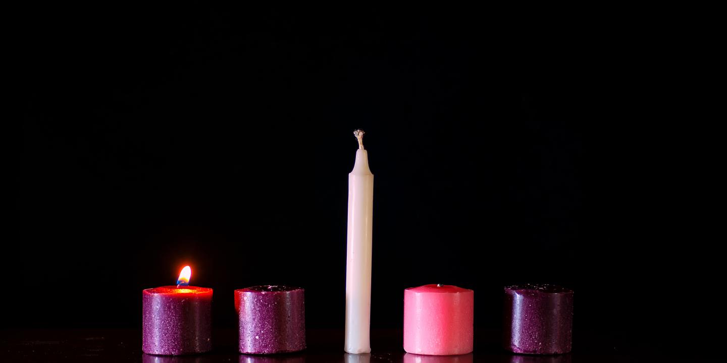 Five candles sit in a row against a dark background, only one is lit.