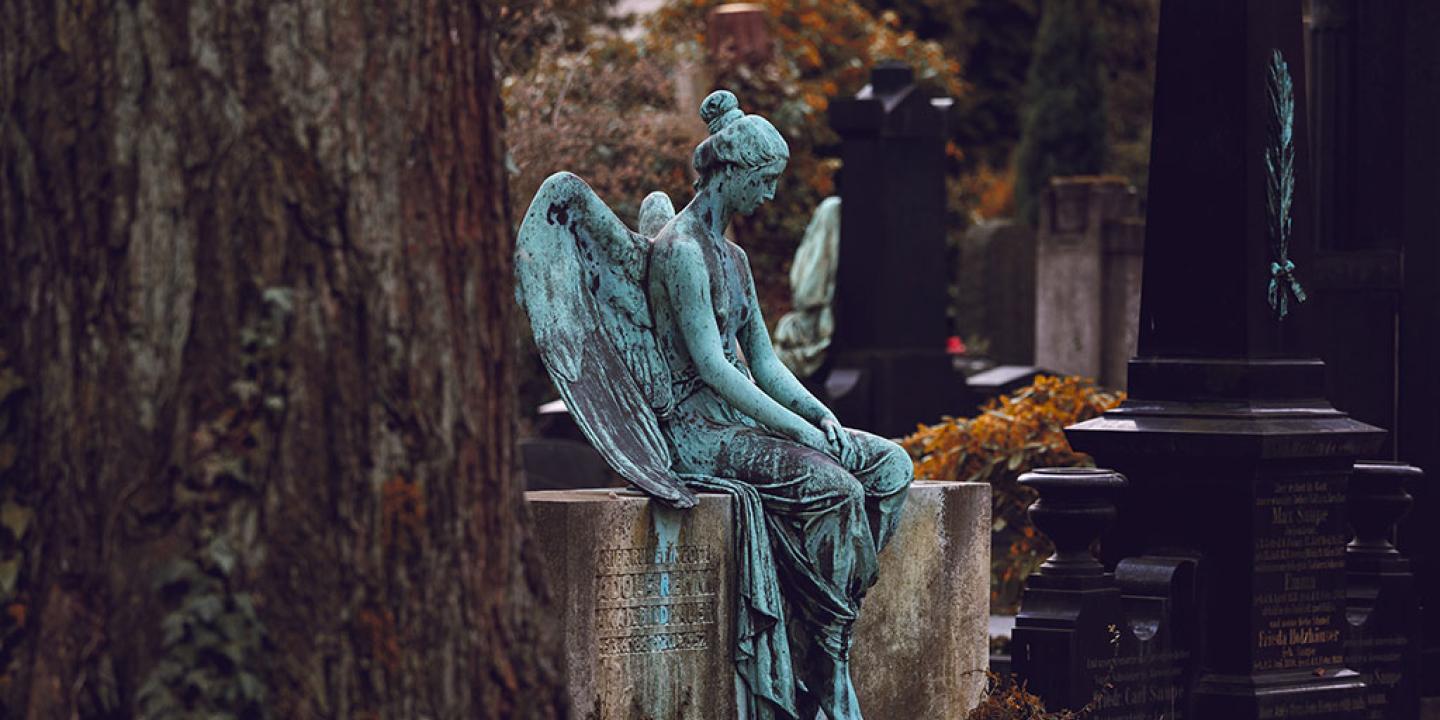 A bronze statue of a resting angel sits atop a low stone grave.