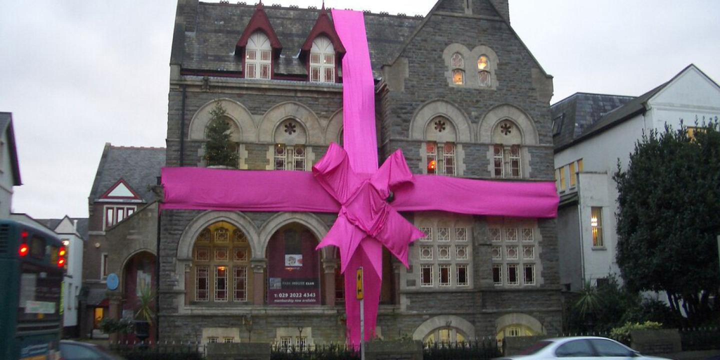 A large stone house is wrapped in a red ribbon and bow.