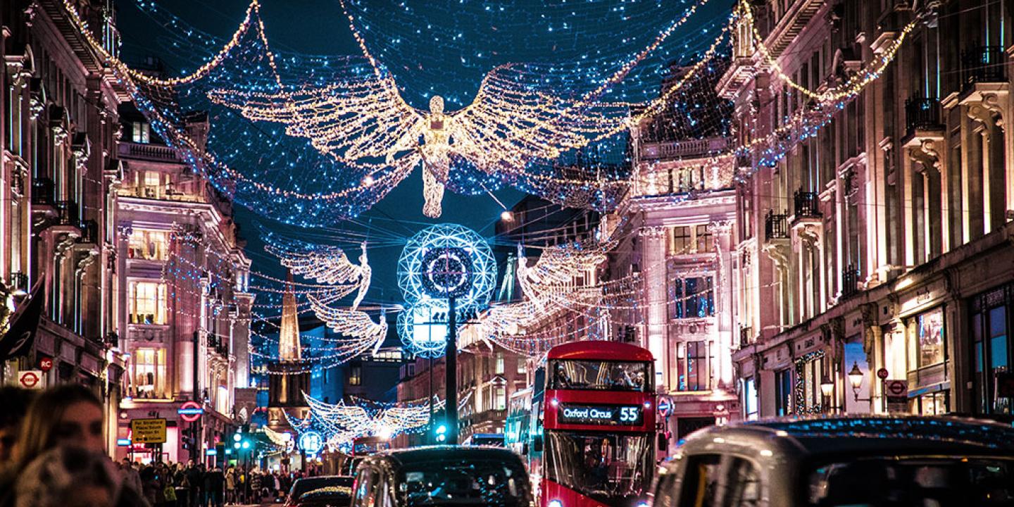 A shopping street is crowded by taxi cabs and buses while above it a Christmas illumination of an angel hangs over all.