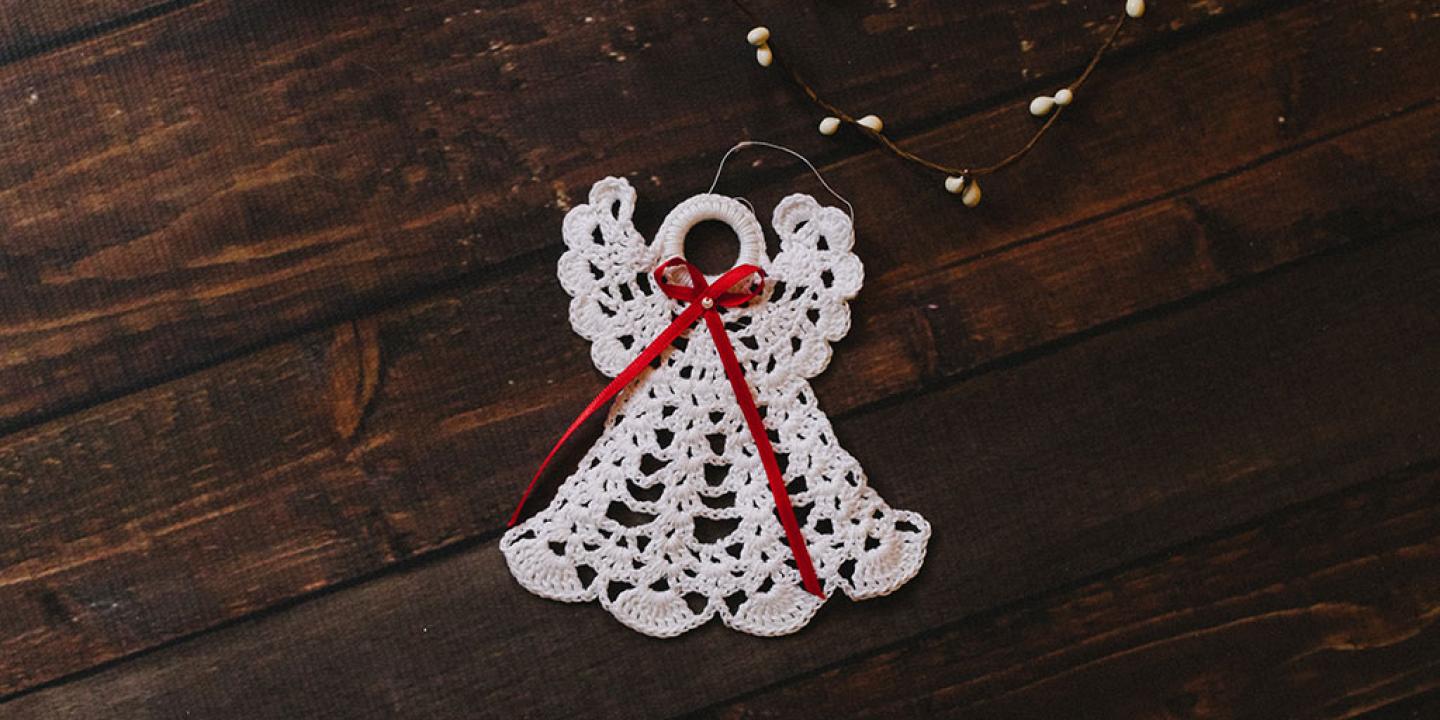 A white crocheted angel decoration against a dark background.