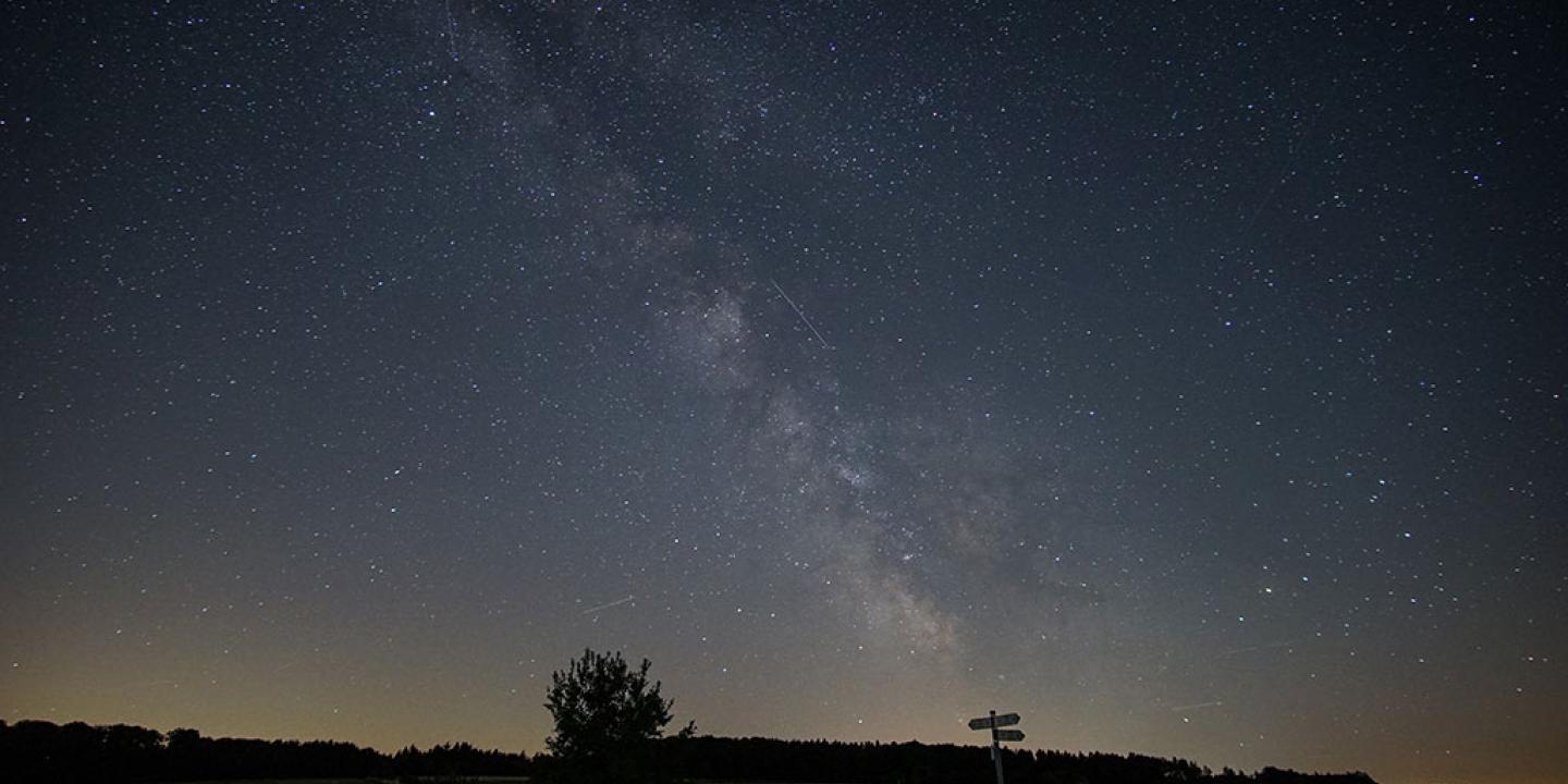 A starry night sky below which a signpost is silhouetted.