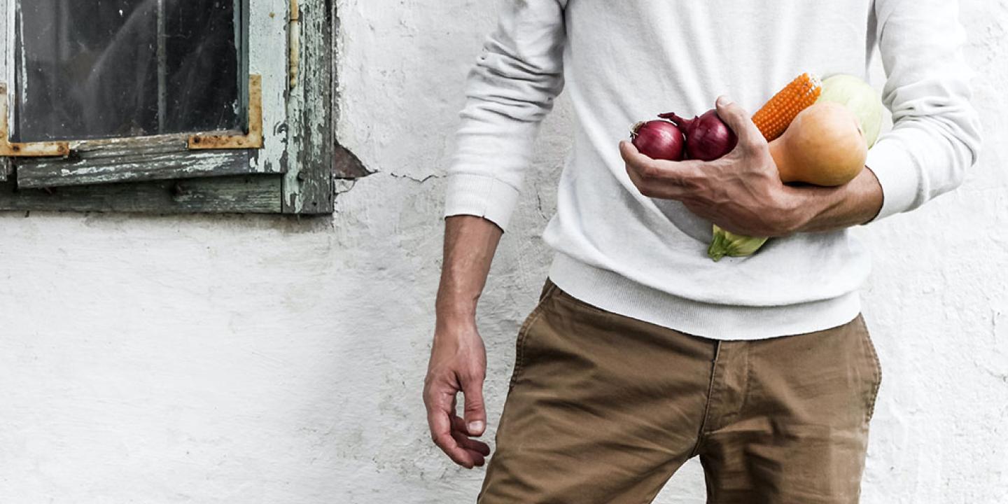 A man stands at rest, one arm holding some vegetables.