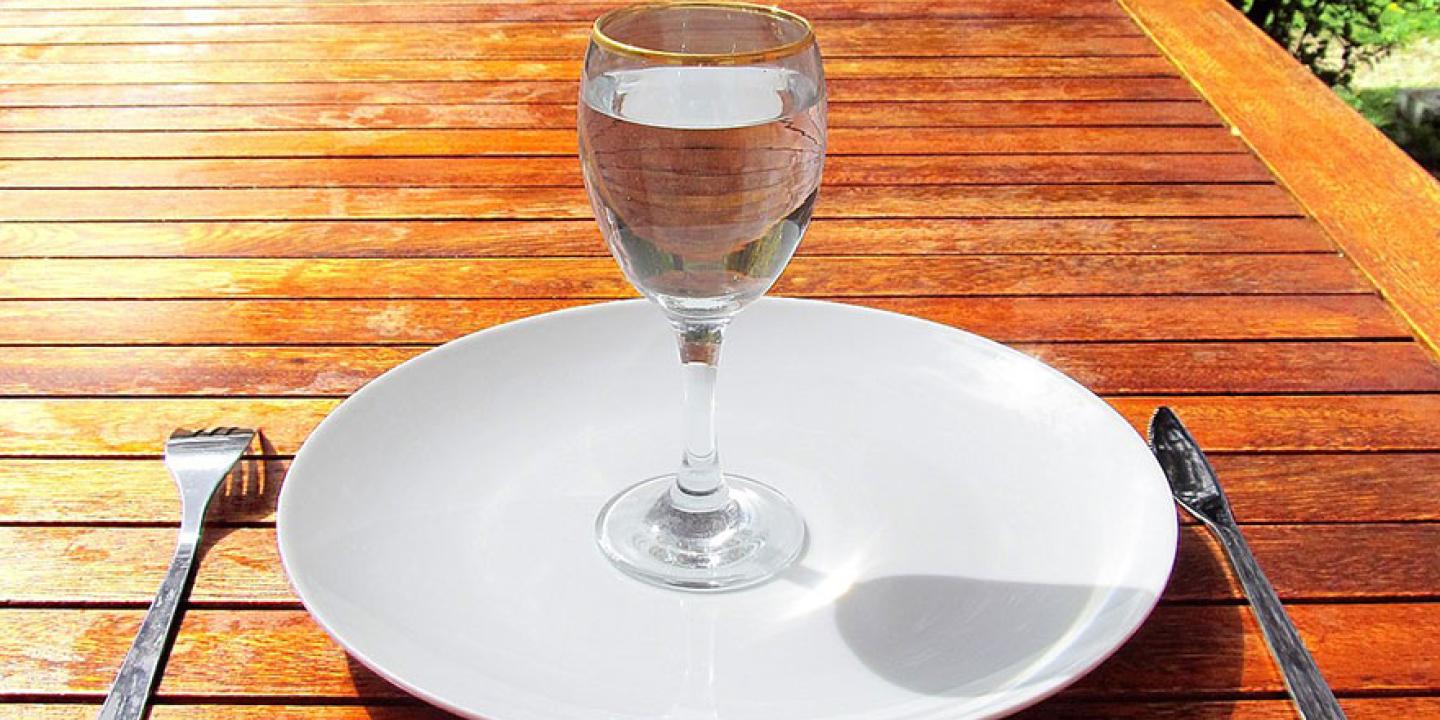 A wine glass of water sits on an empty clean plate.