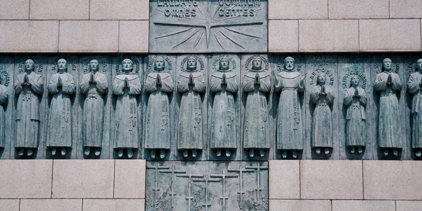 A stone monument within which set, in the shape of a cross are statues of numerous standing praying figures.