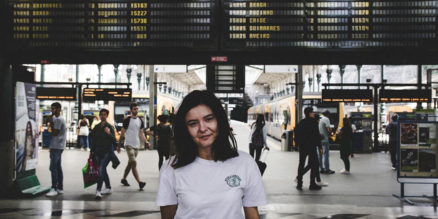 A young person stands in front of railway station platfrorms and below a large informaton display.