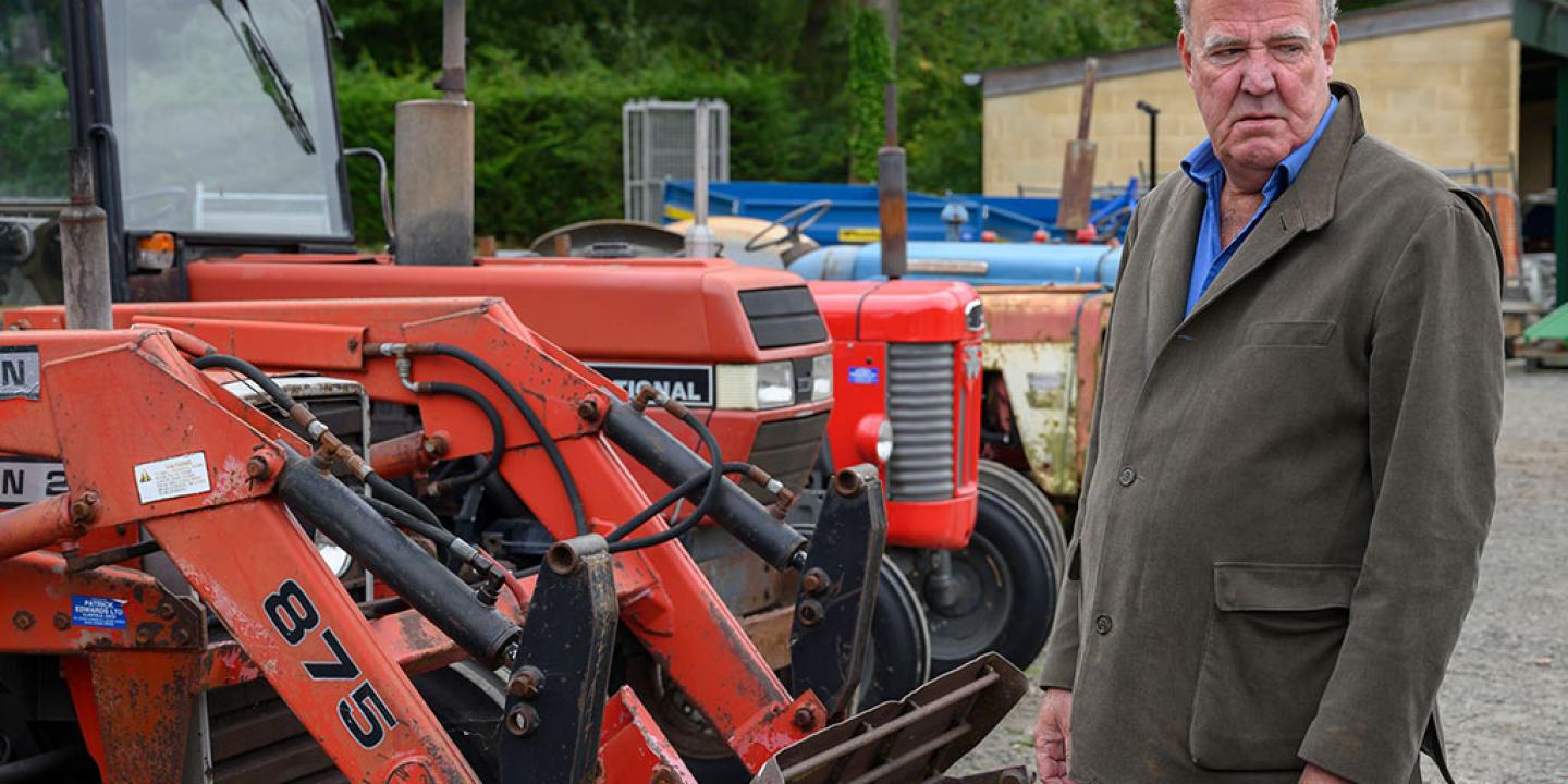 A man stands looking baleful next to a row of red tractors