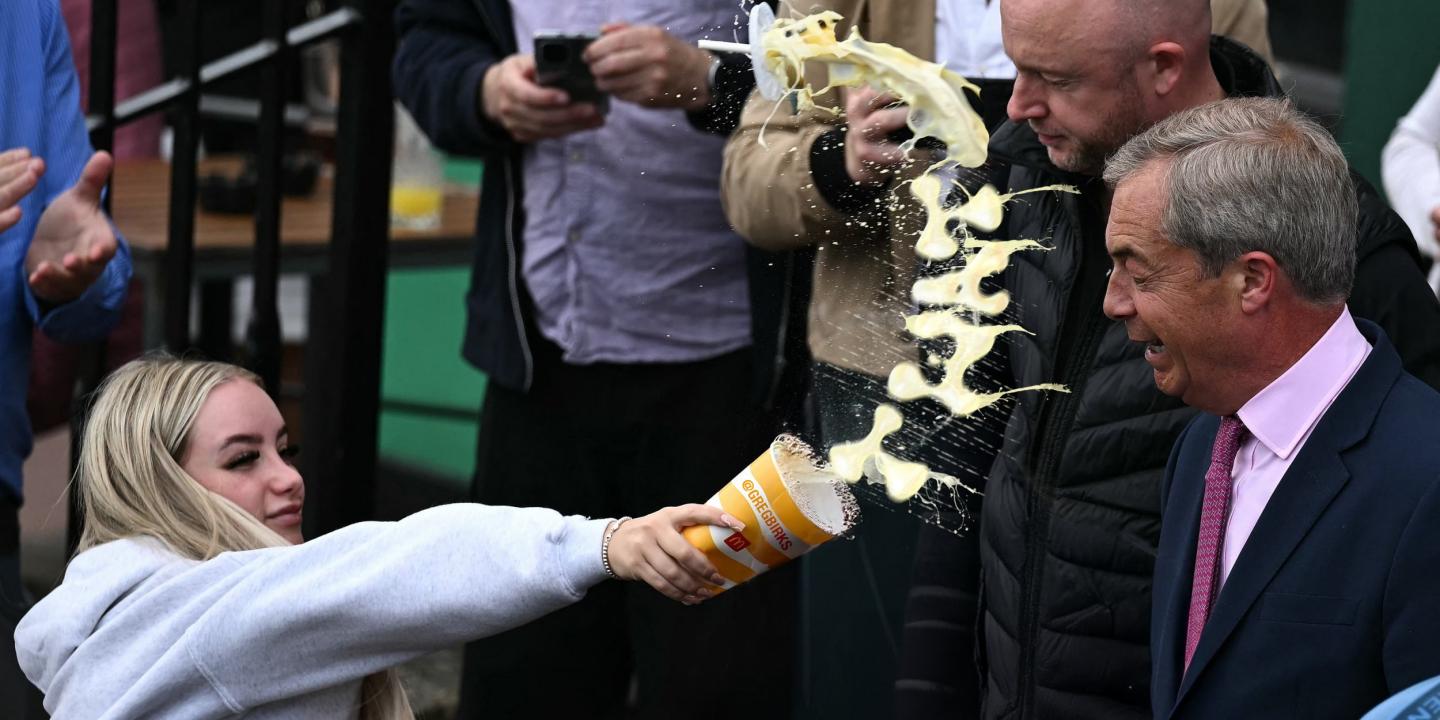 A woman throws a milkshake at a politician, the milk is mid-flight in a curved shape.