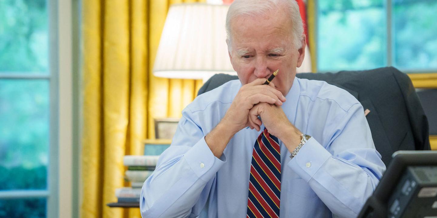 President Biden sits at a desk, holding his balled hands to his mouth.