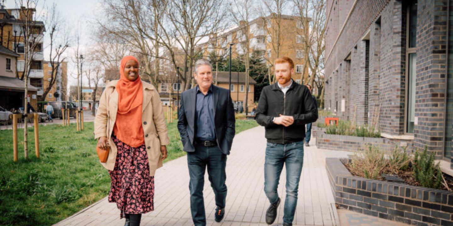 Kier Starmer walks along a residential development's path with two other people.