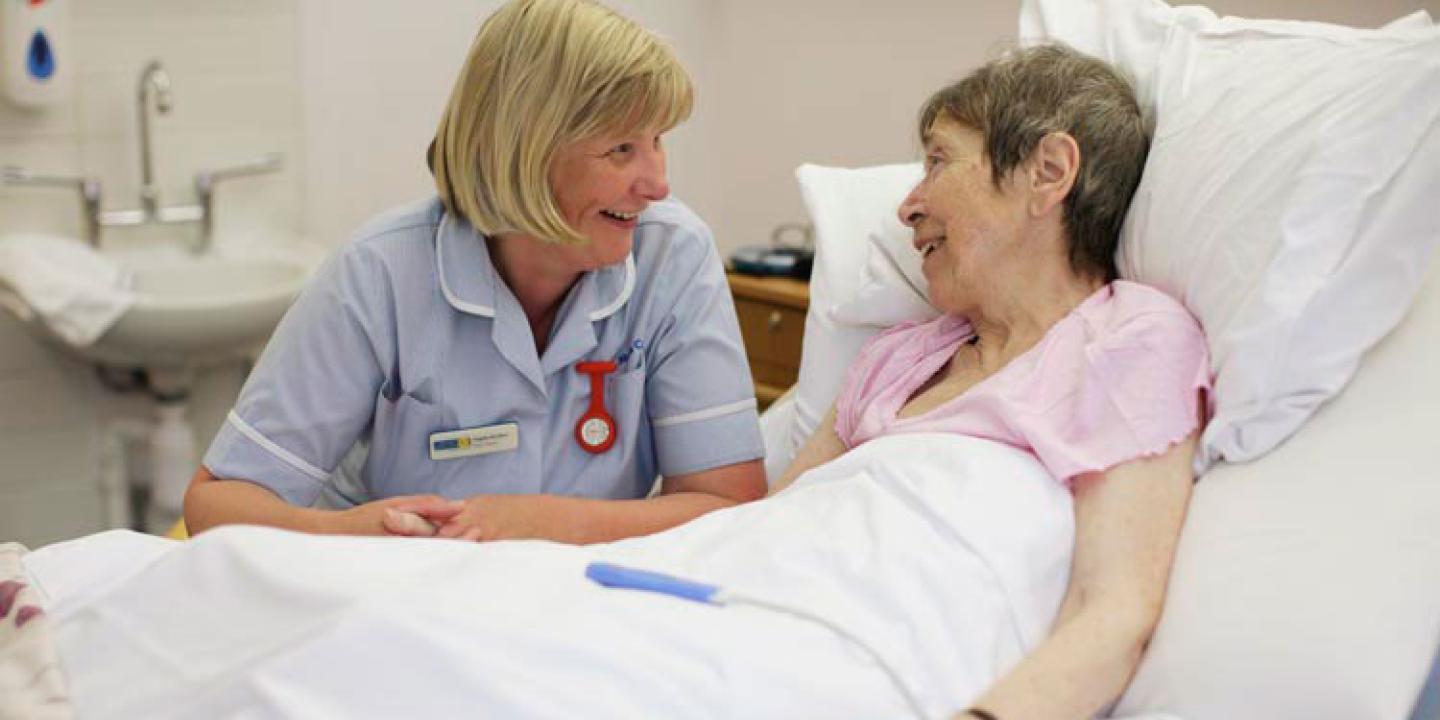 A nurse bends beside a bed and talks to a patient