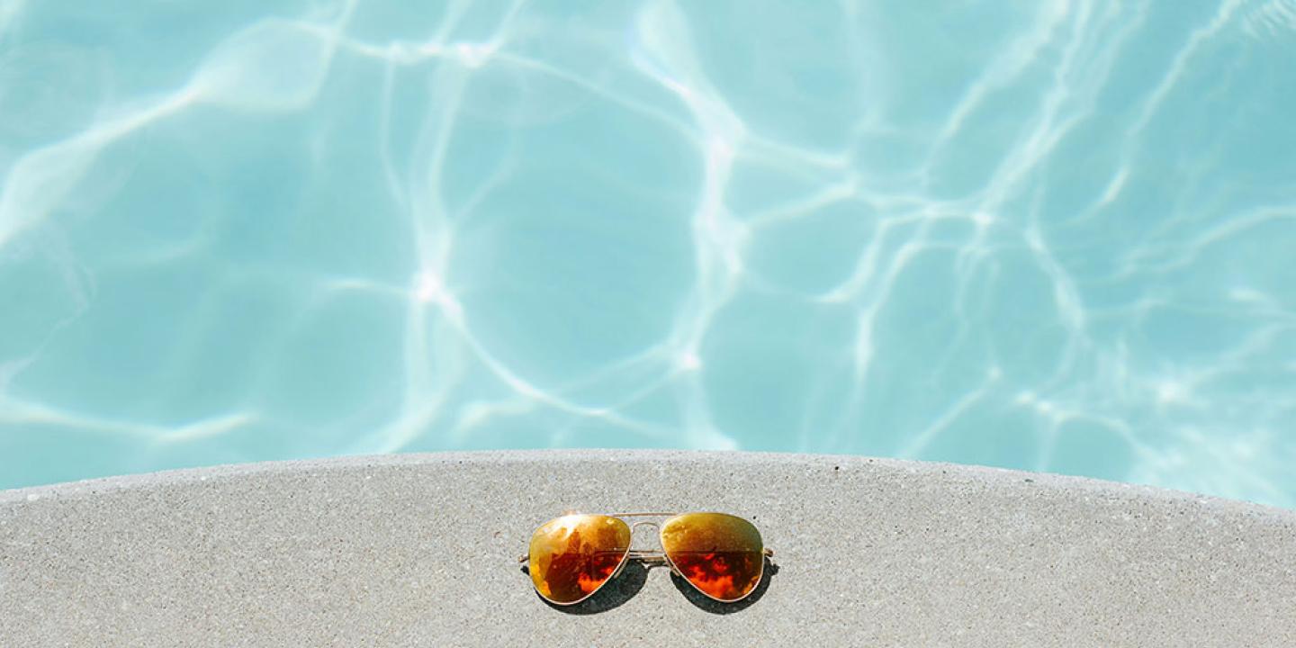 A pair of sunglasses beside a swimming pool.