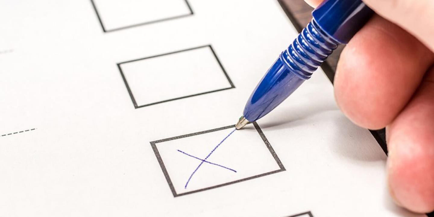 A pen draws a cross in a box on a ballot form.