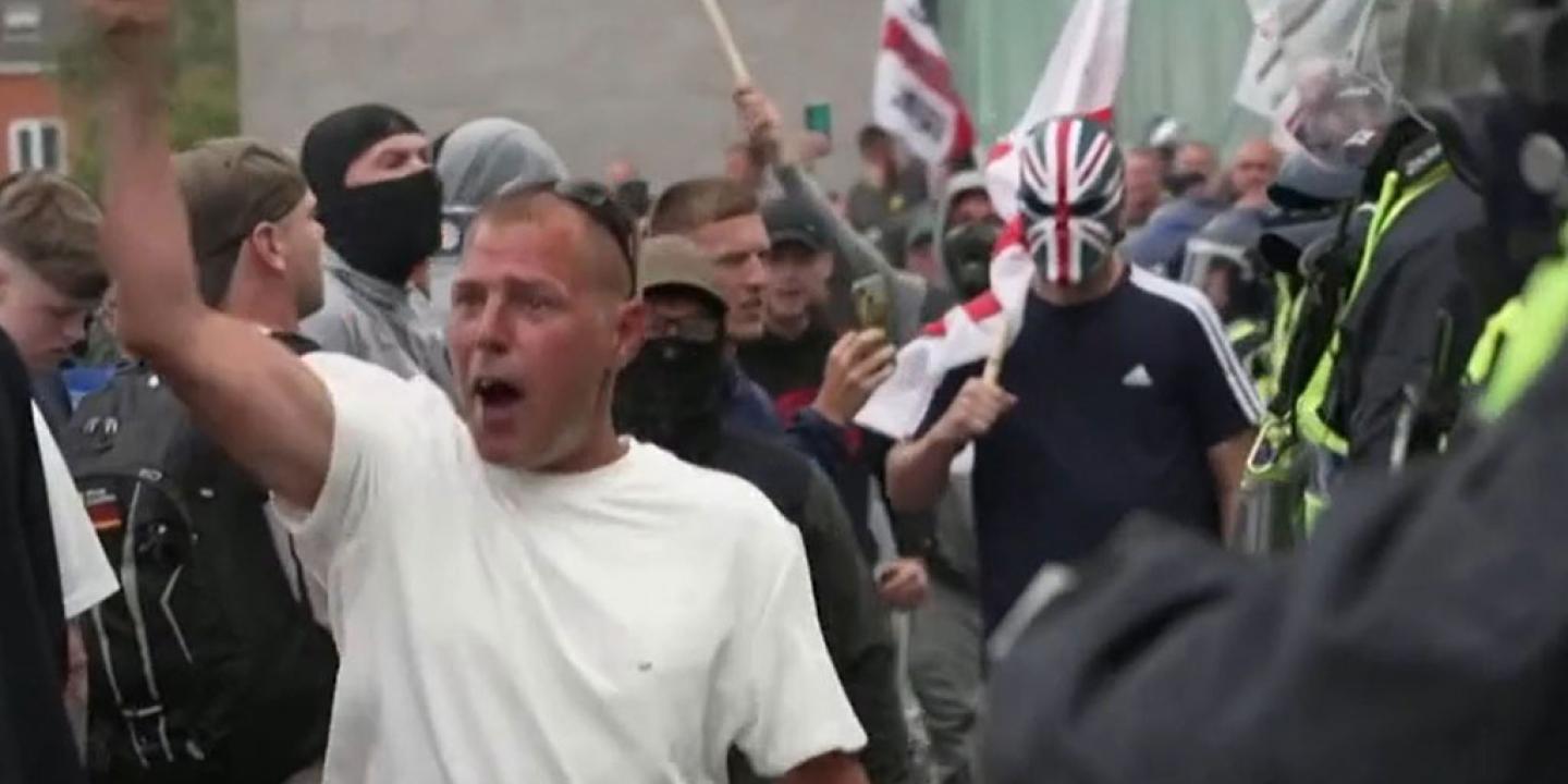 Rioters confront police, one wearing a sinister Union Jack mask