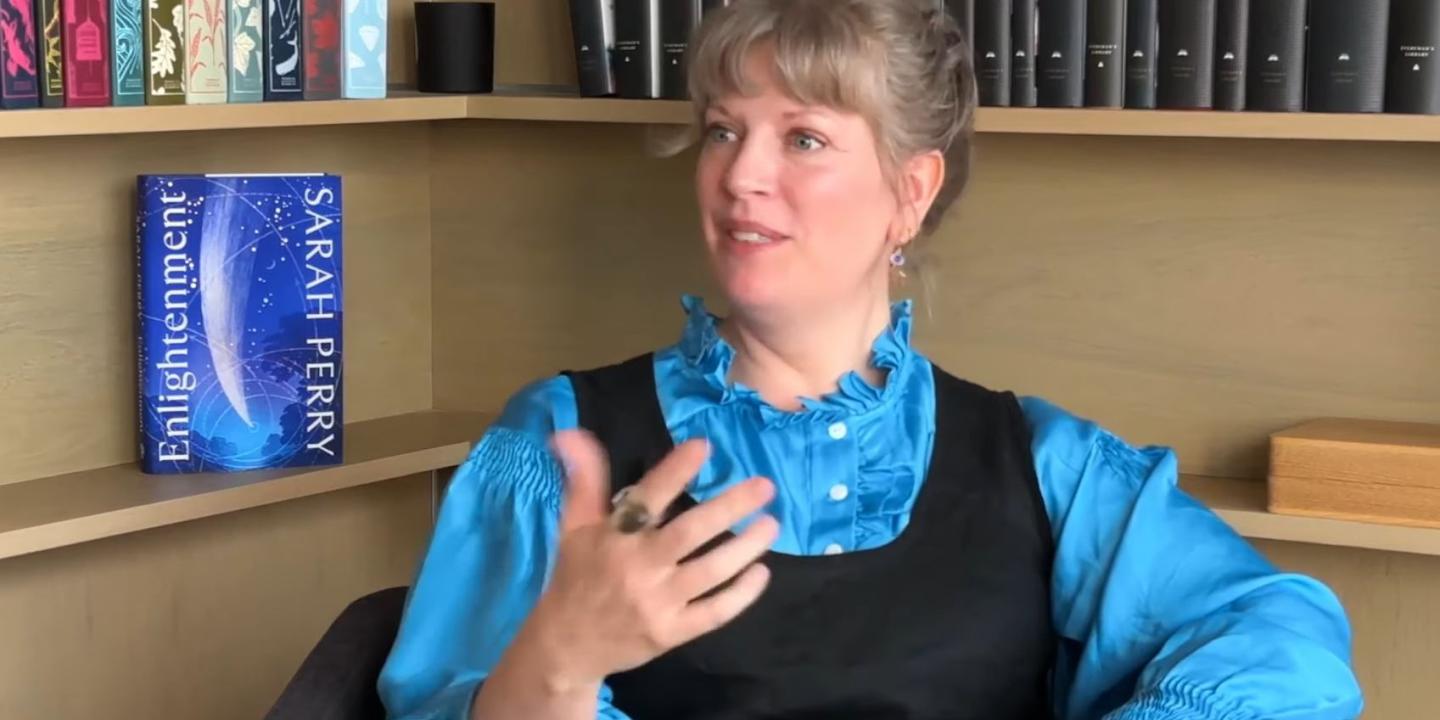 A woman being interviewed gestures with a hand in front of her