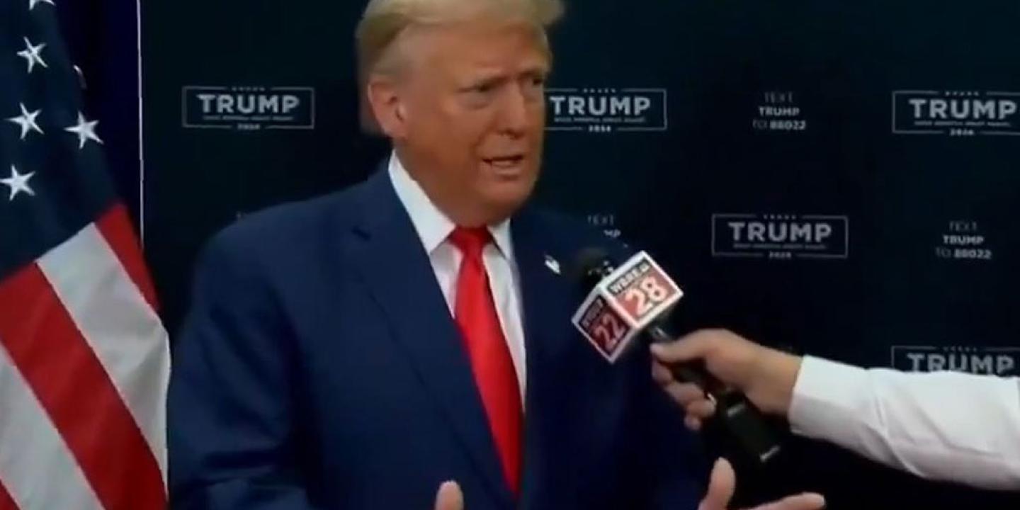 Donald Trump gestures with his hands while someone holds a mic in front of him,