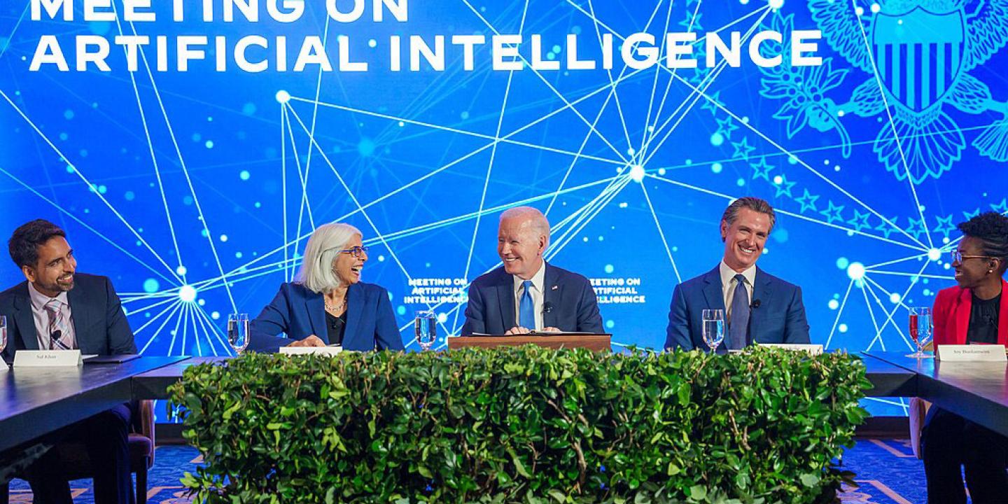 A board of experts sit at a table against a conference backdrop.